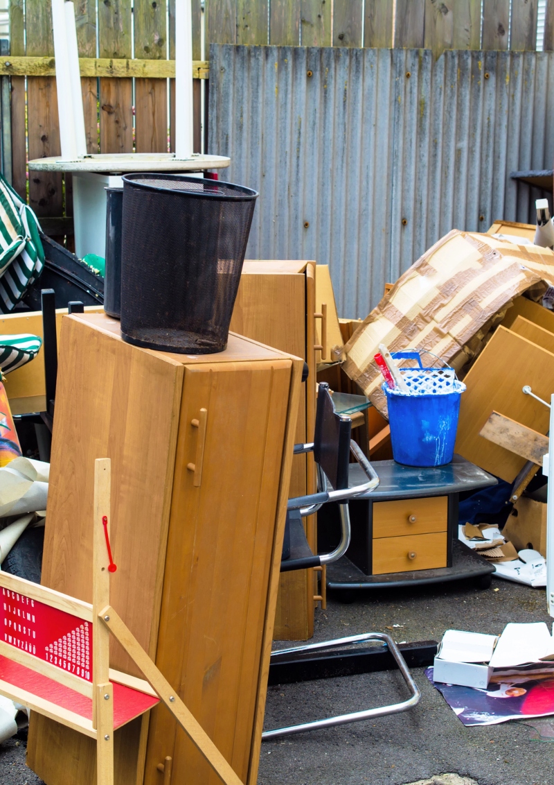 A pile of junk, including old furniture, a child's play set, and a trash can, blocking a driveway