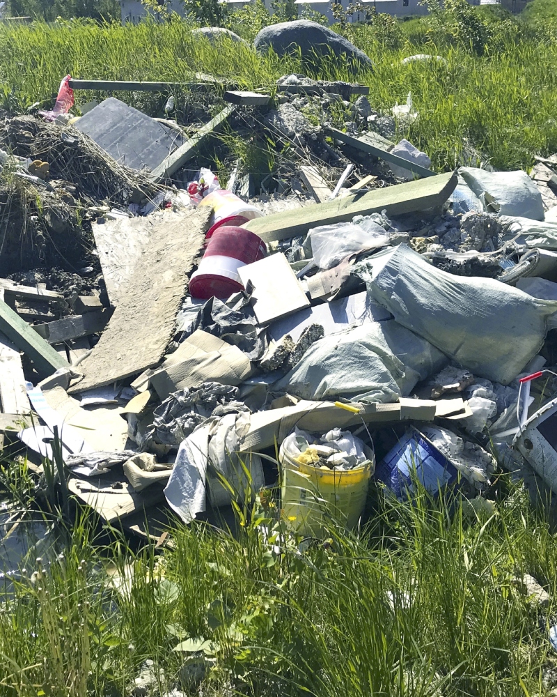 An eyesore of discarded items, including construction materials and household waste, polluting a beautiful landscape