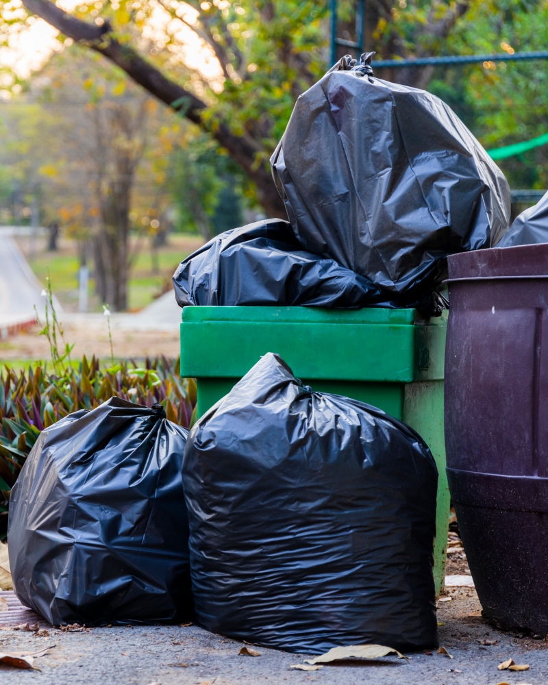 Trash cans overflowing with garbage bags and loose debris