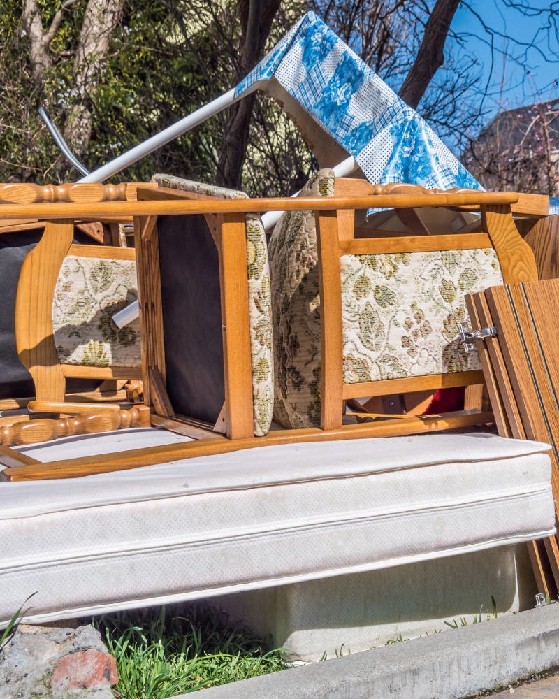A messy pile of discarded furniture, including a mattress, chairs, and a table frame