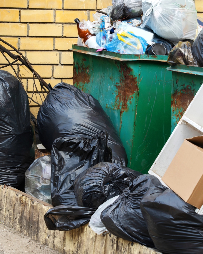 A pile of trash bags and loose trash spilling out of full trash cans
