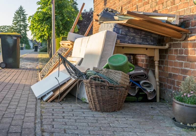 A messy pile of discarded furniture, including a mattress, chairs, a table, and a watering can